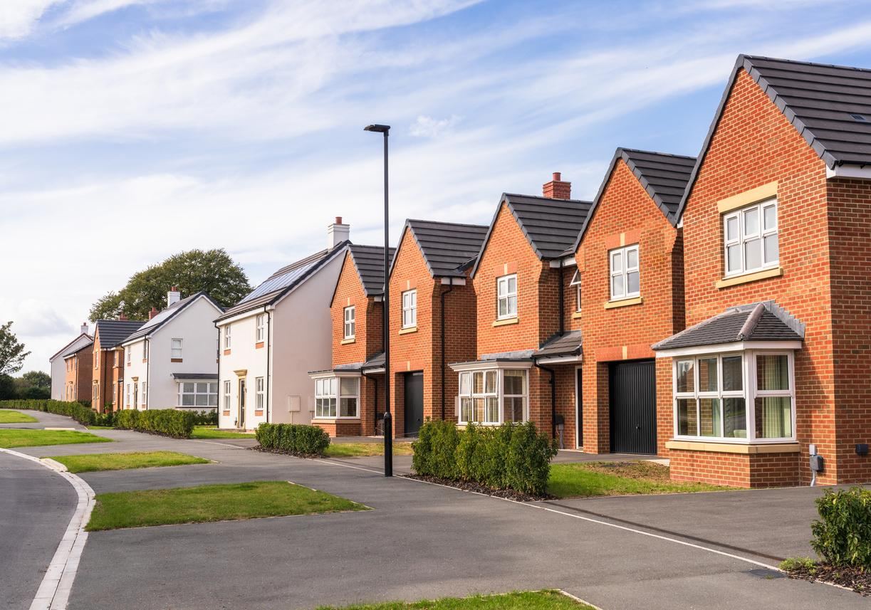 A row of newly built brick family homes with bay windows on a landscaped residential street.